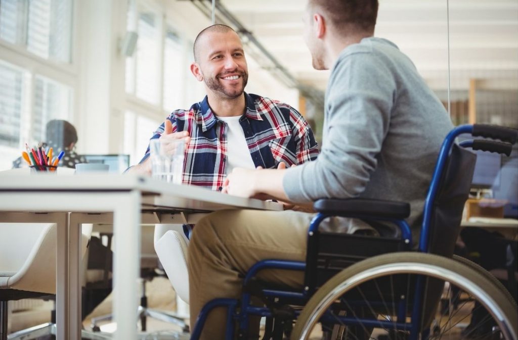 A disabled man in a wheelchair sat at a table with a friend having a chat